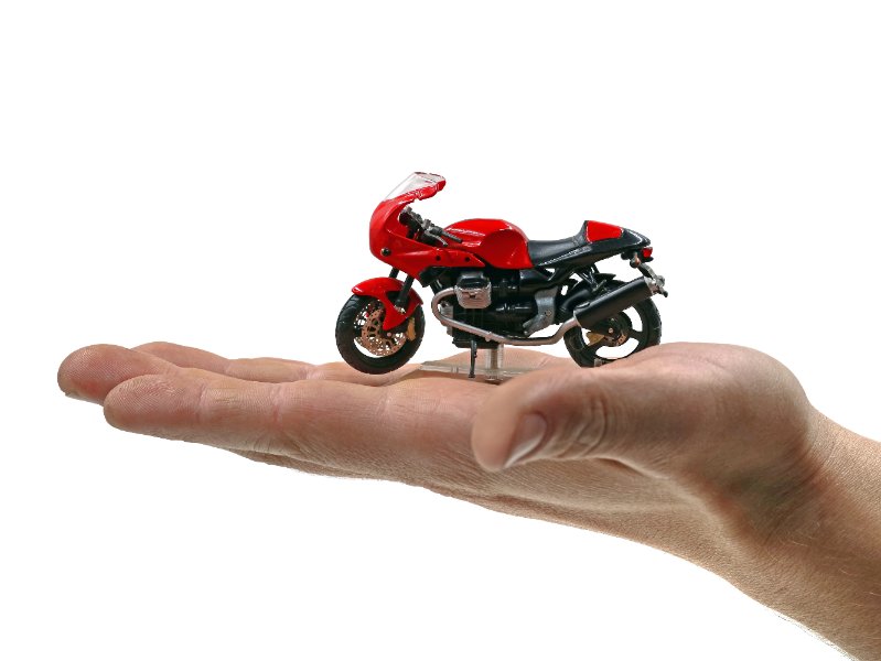 Moto miniature rouge posée de profil sur la paume d’une main